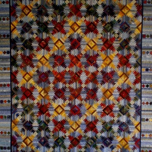 May include: A quilt with a geometric pattern of triangles in shades of blue, red, yellow, and brown. The quilt is made of fabric scraps and has a patchwork design.