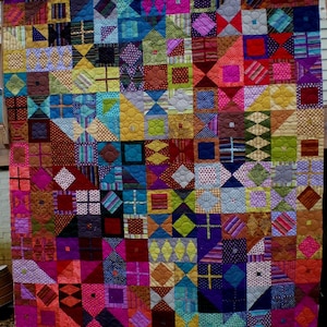 Puede incluir: Una colcha colorida con una variedad de patrones geométricos y colores brillantes, incluyendo rojo, rosa, morado, azul, verde, amarillo y marrón.