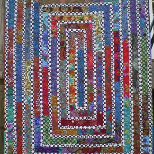 May include: A colorful quilt with a geometric pattern of concentric squares and circles. The quilt is made of various fabrics with different patterns and colors, including red, blue, green, and brown.