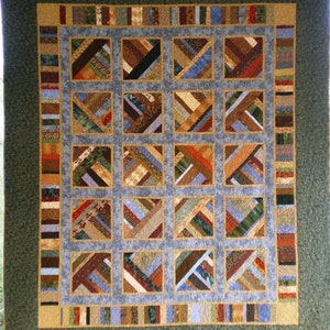 May include: A quilt with a patchwork design featuring a variety of fabrics in shades of brown, blue, and green. The quilt is made up of 16 squares, each with a different pattern. The quilt is framed by a border of brown, blue, and green fabric.