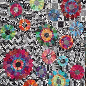 May include: A black and white quilt featuring colourful flower designs. The quilt is made up of various geometric shapes and patterns. The flowers are in shades of red, orange, yellow, green, blue, and purple.