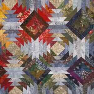 K&ouml;nnte beinhalten: Eine Decke aus verschiedenen bunten Stoffresten in Blaut&ouml;nen, Rot, Gr&uuml;n und Braun. Die Decke ist im Ananas-Muster mit einem geometrischen Design gefertigt.