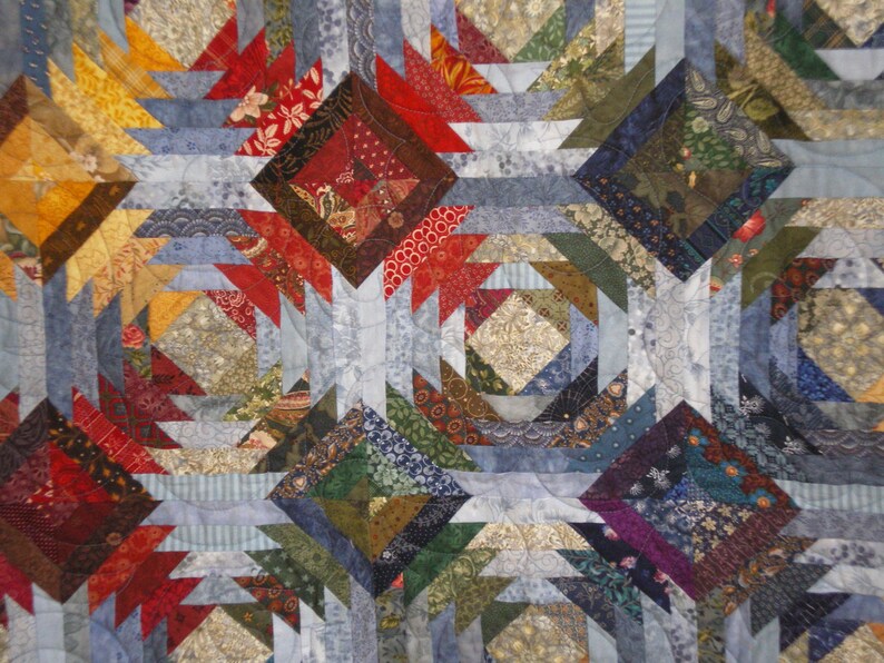 K&ouml;nnte beinhalten: Eine Decke aus verschiedenen bunten Stoffresten in Blaut&ouml;nen, Rot, Gr&uuml;n und Braun. Die Decke ist im Ananas-Muster mit einem geometrischen Design gefertigt.