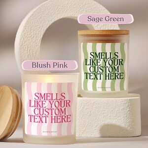 Puede incluir: Dos velas de vidrio esmerilado con tapas de madera. Una vela tiene una etiqueta ondulada rosa y blanca, la otra una etiqueta ondulada verde y blanca. Ambas velas tienen el texto "SMELLS LIKE YOUR CUSTOM TEXT HERE".