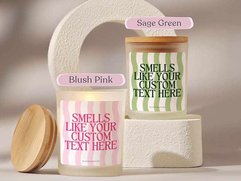 Puede incluir: Dos velas de vidrio esmerilado con tapas de madera. Una vela tiene una etiqueta ondulada rosa y blanca, la otra una etiqueta ondulada verde y blanca. Ambas velas tienen el texto "SMELLS LIKE YOUR CUSTOM TEXT HERE".