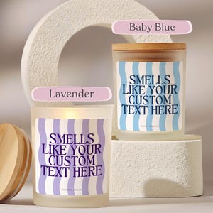 Puede incluir: Dos velas de vidrio esmerilado con tapas de madera. Una vela est&aacute; etiquetada como "Baby Blue" y la otra como "Lavender". Ambas velas tienen etiquetas con el texto "Smells Like Your Custom Text Here" en un patr&oacute;n ondulado.
