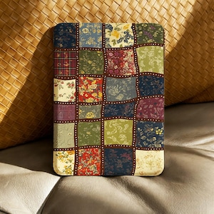May include: A tablet case with a patchwork design. It features squares of floral and plaid patterns in red, blue, green, and yellow. The case has a brown border with small white dots.