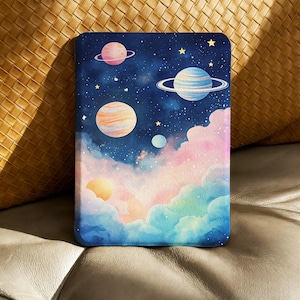 以下が含まれることがあります： 惑星、星、カラフルな雲が描かれた星空の、水彩画イラストが施された長方形のケース。惑星はピンク、オレンジ、青など様々な色で描かれています。雲はピンク、青、黄色の混合色です。