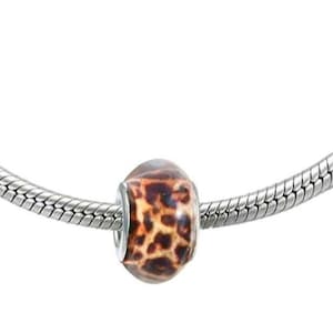 May include: A silver bracelet featuring a charm. The charm is a bead with a brown and tan leopard print pattern. The bracelet has a snake chain design.