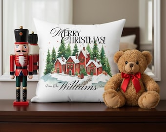 May include: A white decorative pillow with a Christmas village scene and the text "MERRY CHRISTMAS!" and "From The Williams Fam". A brown teddy bear with a red bow sits next to the pillow. A red and black nutcracker stands to the left.