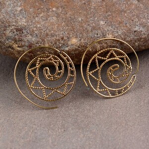 May include: A pair of gold spiral earrings. Each earring has a spiral design with a star pattern in the centre. The earrings are displayed on a neutral surface.