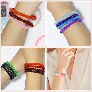 May include: A collection of beaded bracelets in various colors, including red, orange, pink, purple, blue, green, and black. The bracelets are shown stacked on wrists, showcasing the different color options and styles. The beads appear to be small and round.