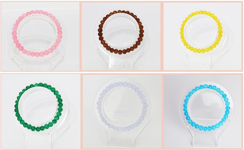 May include: Six beaded bracelets in various colors: pink, brown, yellow, green, lavender, and blue. Each bracelet is displayed on a clear, circular stand, showcasing the round beads. The bracelets are likely for wrist wear.
