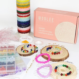 May include: A collection of colorful beaded bracelets and jewelry-making supplies. The image includes a pink box with the text "WOOLEE" and "INSPIRE CREATIVITY AND LOVE WITH BEADS". There are also spools of string and a container of beads.