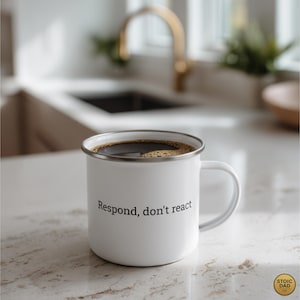 May include: White enamel mug filled with coffee, featuring the text "Respond, don't react" in black. The mug has a silver rim and a white handle. The mug is on a countertop.