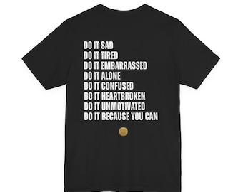 May include: Black t-shirt with white text: "DO IT SAD, DO IT TIRED, DO IT EMBARRASSED, DO IT ALONE, DO IT CONFUSED, DO IT HEARTBROKEN, DO IT UNMOTIVATED, DO IT BECAUSE YOU CAN." A small gold circle is at the bottom.