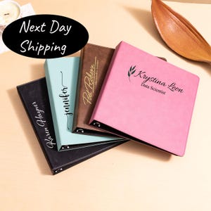 May include: A collection of personalized binders in various colors: black, light blue, brown, and pink. Each binder features a name or text in elegant script. The text "Next Day Shipping" is in a black oval.