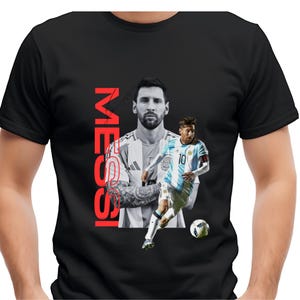 May include: Black t-shirt featuring a graphic of a soccer player in an Argentina jersey. The word "MESSI" is printed vertically in red. The design includes two images of the player, one in black and white and the other in color.