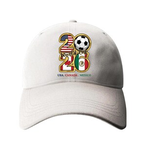 May include: White baseball cap featuring a gold-framed "26" design with a soccer ball, the American and Mexican flags. The text "USA. CANADA. MEXICO" is printed below the design. A stylish accessory for soccer fans.