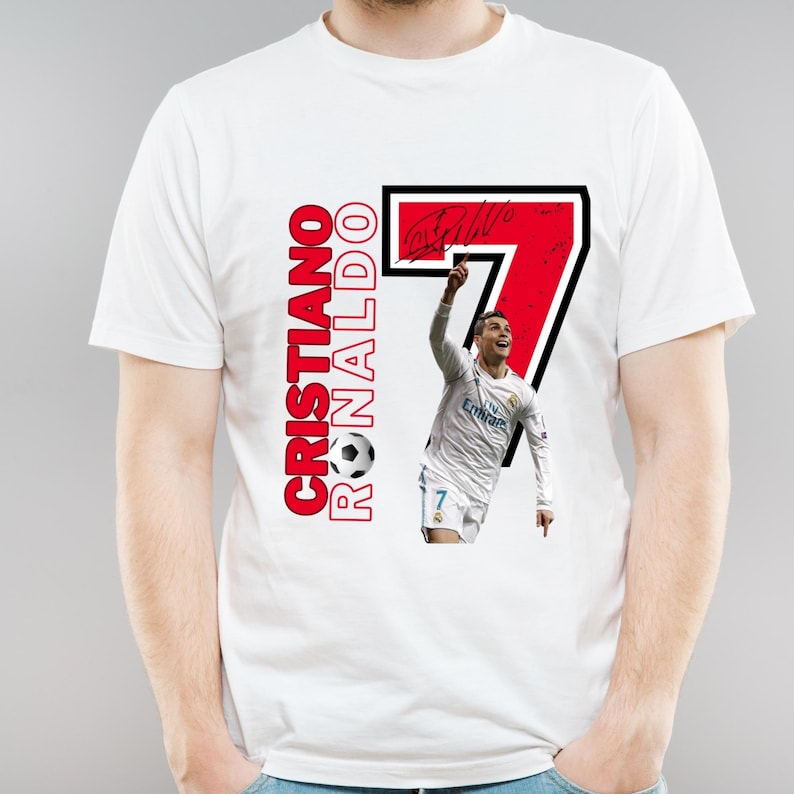 May include: White t-shirt featuring a graphic of Cristiano Ronaldo with the number 7 in a black and red design. The text "Cristiano Ronaldo" is printed vertically in red with a soccer ball graphic.