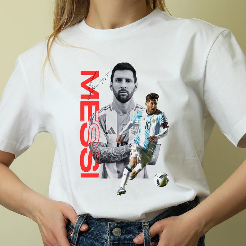 May include: White t-shirt featuring a graphic of a soccer player in a blue and white uniform, with the name "MESSI" in red vertical text. The design includes a black and white portrait of the player.