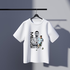 May include: White t-shirt featuring a black and white image of a soccer player, with the name "MESSI" printed vertically on the left side. The design includes two images of the player in action, one in a black and white portrait and the other in color.