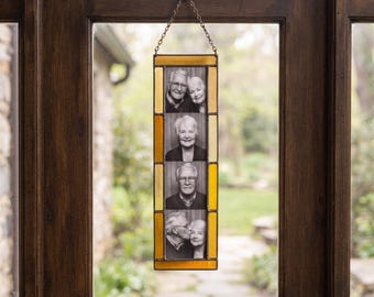 May include: A vertical stained glass photo frame with amber-colored glass borders, suspended by a metal chain. The frame holds four stacked black and white portrait photographs of two individuals, showcasing various poses and expressions in each image.
