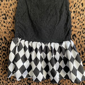Könnte beinhalten: Schwarzer Rock mit strukturiertem Muster auf der oberen Hälfte und einem Harlekinmuster auf der unteren Hälfte. Der Rock hängt an einem Kleiderbügel vor einem Leopardenmuster-Hintergrund.