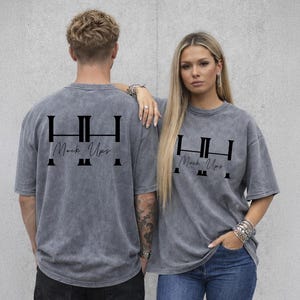 May include: Two people wearing gray, oversized t-shirts with a black graphic on the back that reads "HH Mock Ups." The shirts have short sleeves and a vintage wash appearance. The woman is wearing blue jeans.