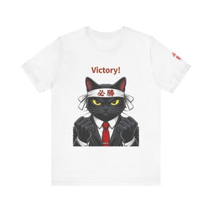 May include: A white t-shirt featuring a graphic of a black cat wearing a suit, a red tie, and a white headband with the Japanese characters 必勝. The word Victory! is printed above the cat, and the cat is shown with clenched fists.