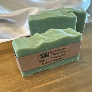 May include: Two bars of green tea and aloe soap from Wild Herb. The soap is all natural and handcrafted. The soap is a light green color and has a rough texture.