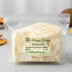 May include: A clear plastic bag containing a block of mango butter. The label reads "Wild Herb Mango Butter All Natural" with the ingredients listed as 100% pure mango butter, and the weight is 907 grams. The website WildHerbSoap.com is also listed.