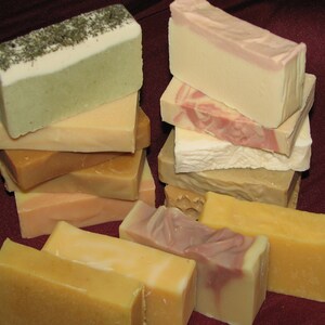 May include: A stack of handmade soap bars in various colors and patterns, including green, white, pink, and brown. The soaps are arranged in a pyramid shape on a red surface.