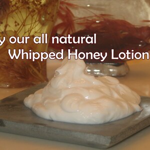 May include: A close-up of a small, white, whipped honey lotion on a gray stone surface. The text "Try our all natural Whipped Honey Lotion!" is visible above the lotion.