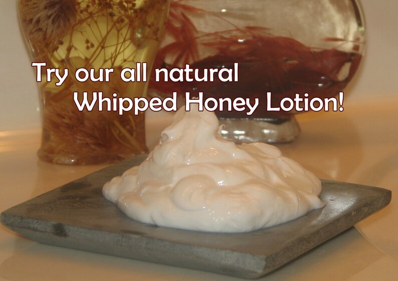 May include: A close-up of a small, white, whipped honey lotion on a gray stone surface. The text "Try our all natural Whipped Honey Lotion!" is visible above the lotion.