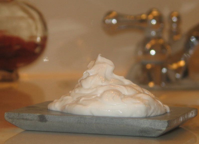 Pode incluir: Um close-up de um creme de barbear branco em um saboneteira de pedra cinza.