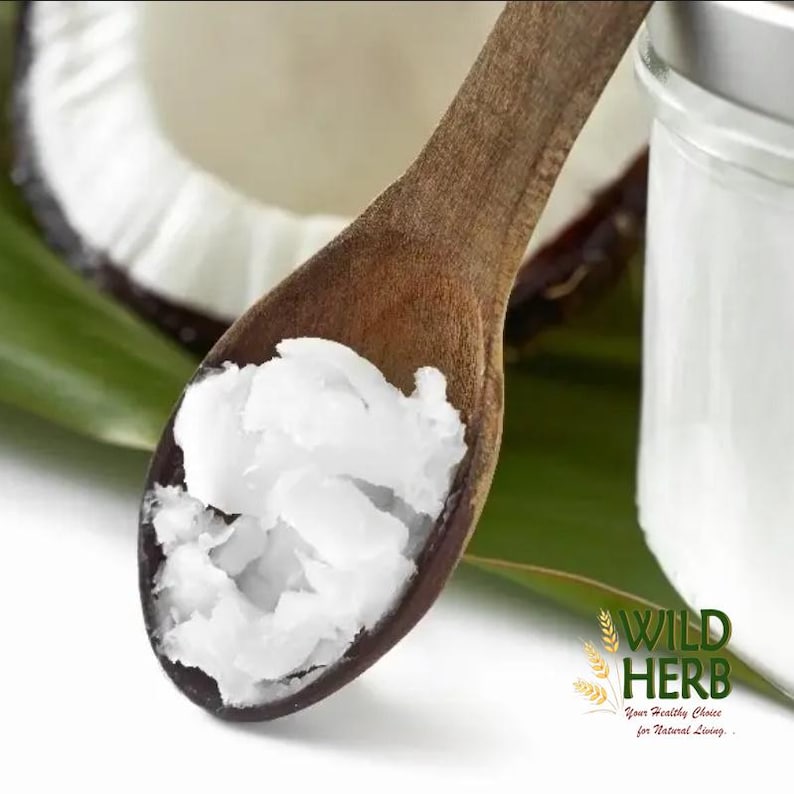 Puede incluir: Una cuchara de madera llena de aceite de coco blanco, con media coco y un tarro en el fondo. La imagen tambi&eacute;n incluye una hoja verde y el texto "WILD HERB Your Healthy Choice for Natural Living."
