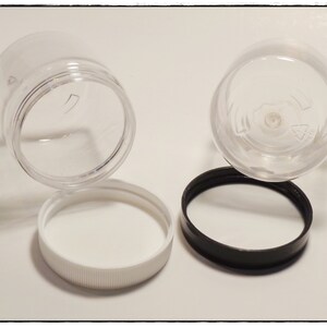 May include: Two clear plastic jars with lids. One jar has a white lid, and the other jar has a black lid.