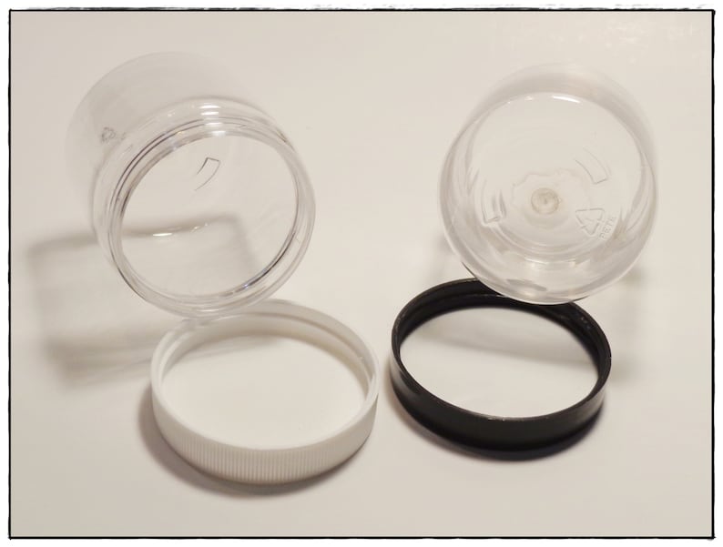May include: Two clear plastic jars with lids. One jar has a white lid, and the other jar has a black lid.