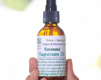 Op de afbeelding: Een bruine glazen fles met een zwarte spuitmond. De fles is gelabeld met "Pure Natural Topical Mineral Spray Rosewood Magnesium Oil" en "herbSoap.com 2 fl. oz. 59 ml".