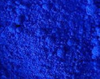 May include: Close-up of a vibrant, deep blue powder. The powder has a fine, granular texture and appears to be evenly distributed. The color is consistent throughout, with no visible variations or patterns. The image is well-lit, highlighting the texture and color of the powder.