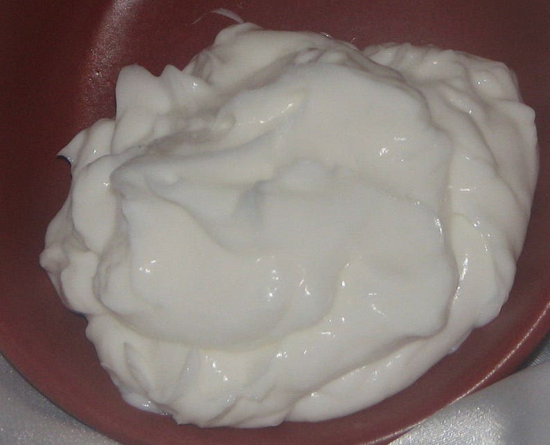 Pode incluir: Um close-up de uma subst&acirc;ncia branca e cremosa, provavelmente iogurte ou creme de leite, em uma tigela vermelha. A subst&acirc;ncia cremosa &eacute; lisa e tem uma superf&iacute;cie ligeiramente texturizada.