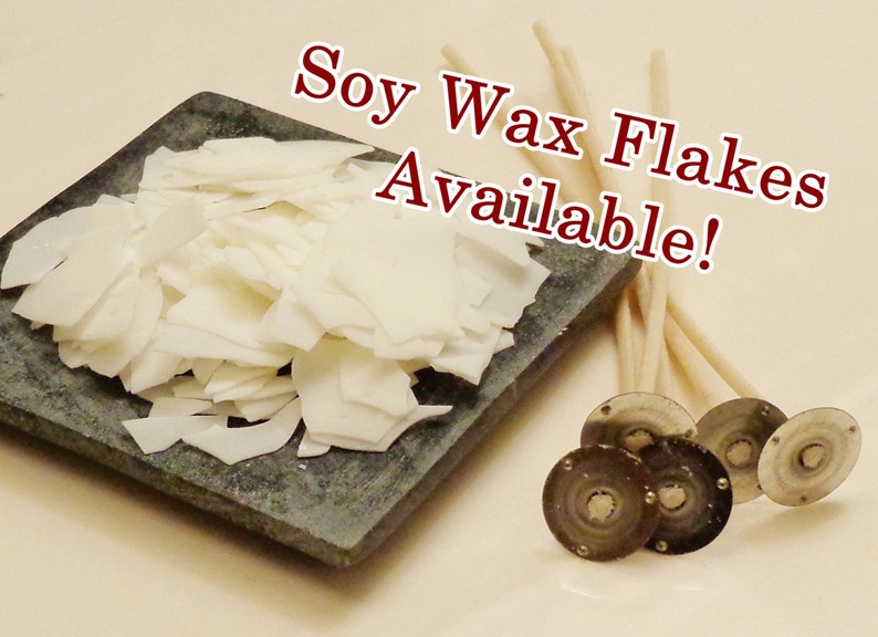 May include: White soy wax flakes on a gray stone surface, next to a bundle of white candle wicks and four silver candle wick stickers. The text "Soy Wax Flakes Available!" is written in red letters on a white background.