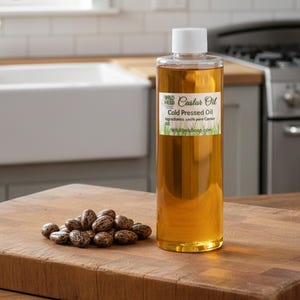May include: A clear bottle of Wild Herb Castor Oil with a white cap, next to a pile of castor beans on a wooden cutting board. The label reads "Castor Oil, Cold Pressed Oil". The background includes a white sink and a kitchen counter.