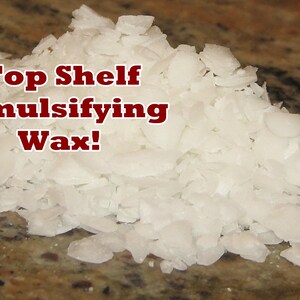 Pu&ograve; includere: Primo piano di cera emulsionante bianca e squamosa. La cera &egrave; in un mucchio su una superficie marrone. Il testo "Top Shelf Emulsifying Wax!" &egrave; scritto in lettere rosse sopra il mucchio di cera.