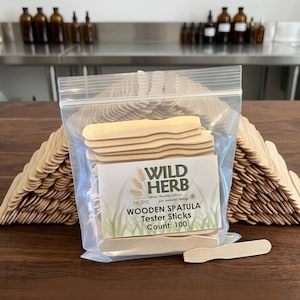 May include: A clear plastic resealable bag filled with light-colored wooden spatula tester sticks. The label reads WILD HERB, Est. 2010, Your healthy choice for natural living, WOODEN SPATULA Tester Sticks, Count: 100. Additional sticks are stacked.