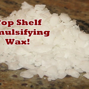 May include: A pile of white emulsifying wax flakes, with the text "Top Shelf Emulsifying Wax!" in red letters. The wax is on a brown and tan speckled surface.