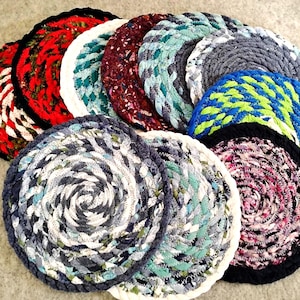 May include: A collection of handmade, circular rag rugs in various colors. The rugs feature a spiral design and are made from braided fabric strips. Colors include red, white, blue, green, and purple. These rugs are suitable for home decor.