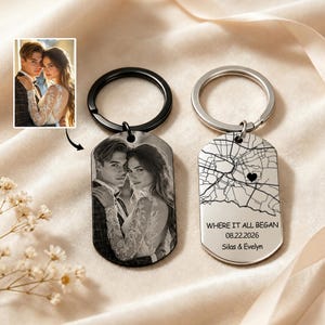 May include: Two metal dog tag keychains. One features a black and white engraved photograph of a couple. The other is silver-toned, displaying a street map with a heart icon, the text WHERE IT ALL BEGAN, the date 22.08.2026, and names Silas & Evelyn.
