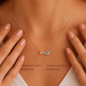 May include: A gold infinity necklace featuring two pear-shaped birthstones, one yellow and one blue. The text below the pendant reads: Customize your birthstone and Customized lover's birthstone, indicating the option for personalised gemstone selection.